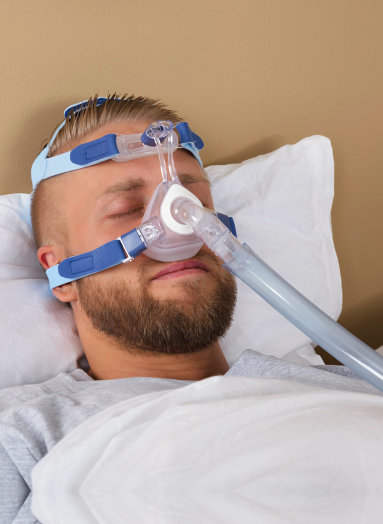 young man lying on bed with sleeping apnea and cpap machine